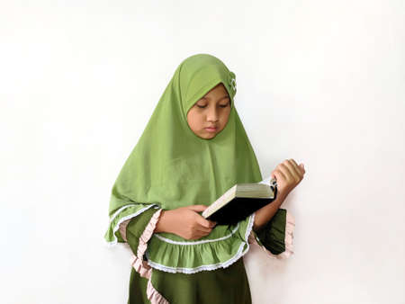 Indonesian Muslim girl holding and reading holy Qurâan in front of a white background, wearing green clothesの写真素材