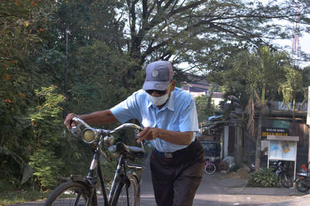 Malang, Indonesia -19 April, 2021: An old Indonesian man pushes his old bicycle on an uphill road in Malang Cityのeditorial素材