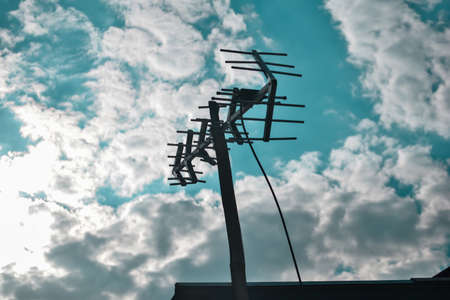 the silhouette of the television antenna above the house which contrasts with the cloudy sky during the dayの写真素材