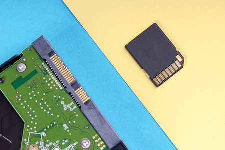 desktop pc hard drive disk or hdd on blue background and small black sd memory card on bright yellow background. pastel colorsの写真素材