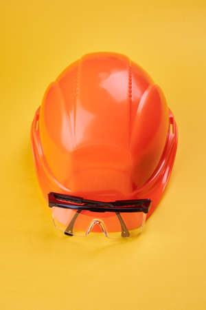 orange protective helmet and safety glasses near it on a bright yellow background. protective workwear and construction industry conceptの写真素材