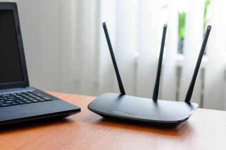 wireless wifi router and laptop at wooden table indoors. window behind. wireless connection concept