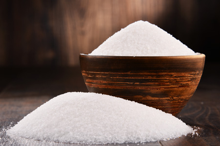 Composition with bowl of white refined sugar on wooden table.