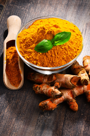 Composition with bowl of turmeric powder on wooden table.
