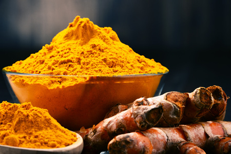 Composition with bowl of turmeric powder on wooden table.