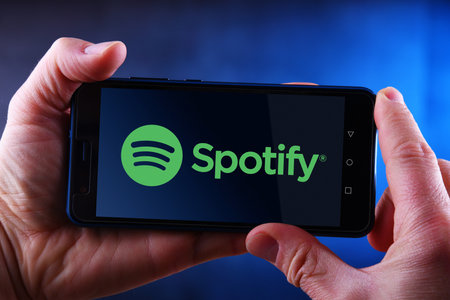 POZNAN, POL - MAR 24, 2019: Hands holding smartphone displaying logo of Spotify, a Swedish audio...