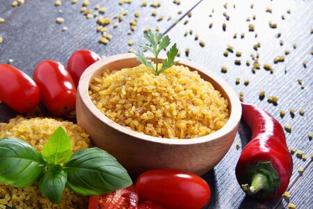 Bowl of uncooked bulgur on wooden table.