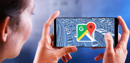 POZNAN, POL - JUL 10, 2019: Woman holding smartphone displaying logo of Google Maps, a web mapping service developed by Googleのeditorial素材