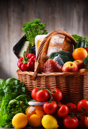 Wicker basket with assorted grocery products including fresh vegetables and fruitsの写真素材