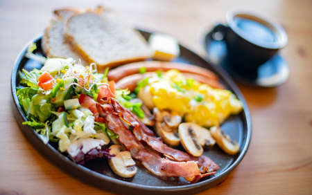 Breakfast with scrambled eggs, bacon, sausages and toast on a restaurant table