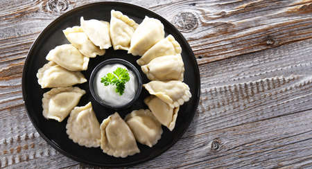 Composition with a plate of classic pierogies with sour cream.
