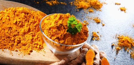 Composition with a bowl of ground turmeric and its fresh rhizome.の写真素材