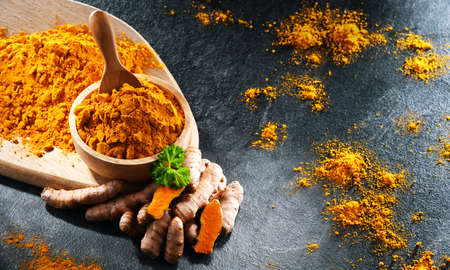 Composition with a bowl of ground turmeric and its fresh rhizome.