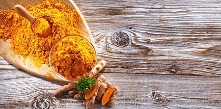 Composition with a bowl of ground turmeric and its fresh rhizome.の写真素材