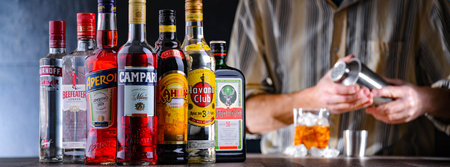 POZNAN, POL - DEC 28, 2021: Bottles of assorted global hard liquor brands and a bartender preparing a drink with a cocktail shakerのeditorial素材