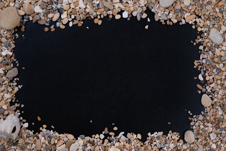 Small sea stones and shells, on a black background, with a free space on the center under the text, title, ad, menu or picture.の写真素材