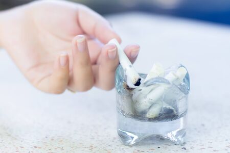 Hand of women drop cigarettes butts in glass ashtray.の写真素材