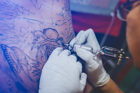 Close up of the tattoo machine. Tattooing. Man creating a picture on his back by a professional tattoo artist.のeditorial素材