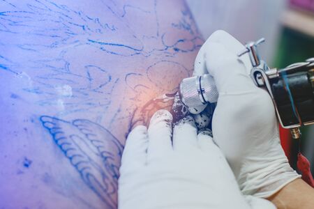 Close up of the tattoo machine. Tattooing. Man creating a picture on his back by a professional tattoo artist.のeditorial素材