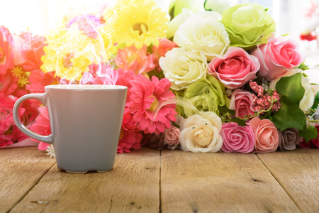 Cup of coffee on a wooden table with flower background under morning sunlight.の写真素材