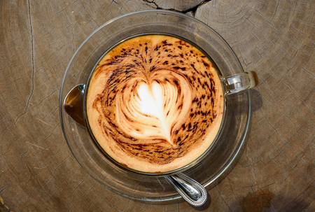 A cup of coffee with heart pattern on wooden background under the morning sunlightの写真素材