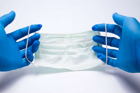 First-person perspective, wearing to a medical blue hand, holding a face mask above the white surface table background Respirator mask for spreading the virus up close,used mask,の写真素材