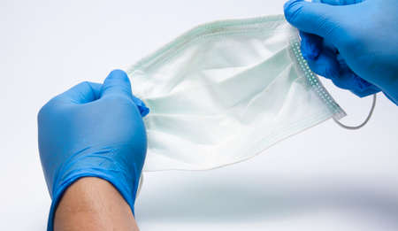 First-person perspective, wearing to a medical blue hand, holding a face mask above the white...
