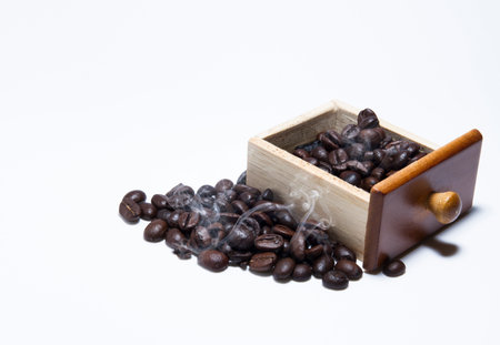 The coffee beans are placed in a wooden box. Beside the wooden box there is another pile of coffee, with smoke floating on the coffee beans in a white background.の写真素材
