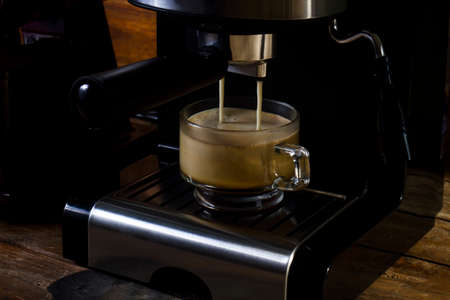Hot espresso flows into the cup. an espresso in a clear glass coffee cup. The background is classic old wood.の写真素材