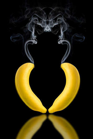 2 bananas, with smoke floating on top Placed in a shape resembling a heart There is a reflection on a black background.の写真素材