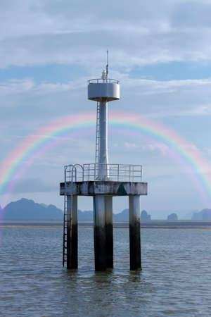 Rainbow occurs at the back of the lighthouse, which is located in the middle of the sea, during which the sea water is dry until the sandbar appears.の写真素材