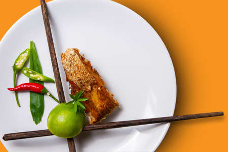 Deep fried sea bass in fish sauce in a white plate. placed side by side with Thai herbs orang background . Top view photoの写真素材