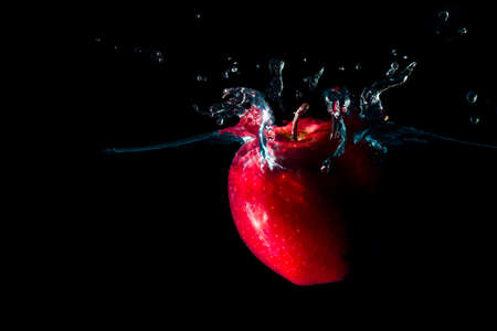 The apple falls into the black water until the sponge splits beautifully on the black background.の写真素材