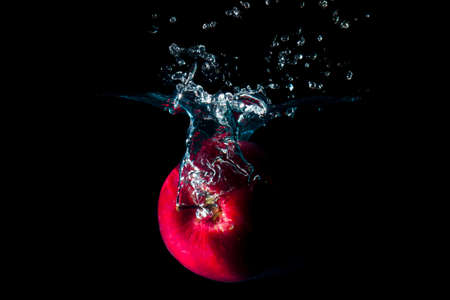 The apple falls into the black water until the sponge splits beautifully on the black background.の写真素材