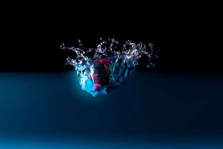 The object falls into the blue water until a sponge splits beautifully on a black background.の写真素材