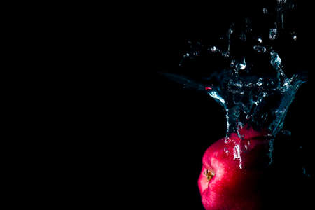 The apple falls into the black water until the sponge splits beautifully on the black background.の写真素材