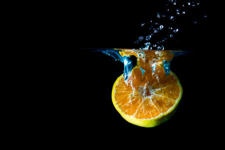 Oranges fall into the  water until the sponge splits beautifully on a black background.の写真素材