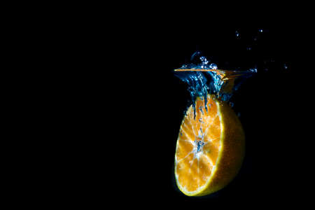 Oranges fall into the  water until the sponge splits beautifully on a black background.の写真素材