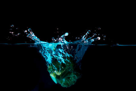 Vegetables fall into the blue water until the sponge splits beautifully on a black background.の写真素材