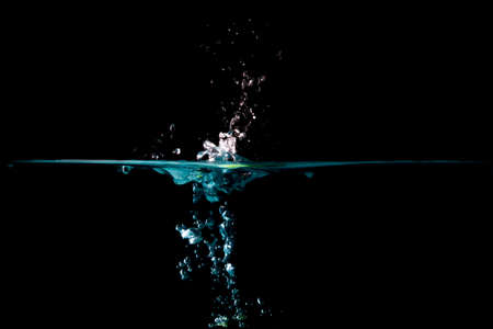 The object falls into the blue water until a sponge splits beautifully on a black background.の写真素材