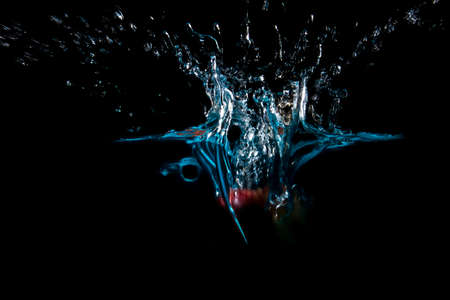 The object falls into the blue water until a sponge splits beautifully on a black background.