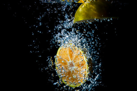 Oranges fall into the  water until the sponge splits beautifully on a black background.の写真素材