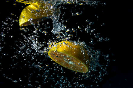 Oranges fall into the  water until the sponge splits beautifully on a black background.の写真素材