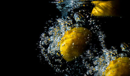 Oranges fall into the water until the sponge splits beautifully on a black background. Summer drink.の写真素材