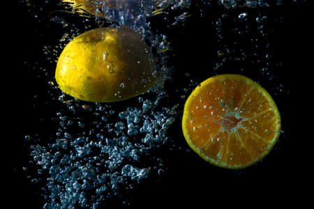 2 oranges fall into the water creating beautiful bubbles. Black background