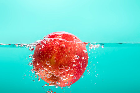 The red apples float in clear water, there are bubbles around the apple. , The apple emerges slightly above the water surface Indigo Green Backgroundの写真素材
