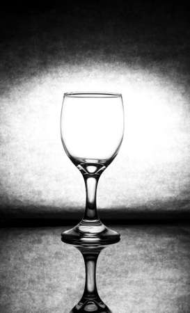 Transparent wine glass, placed on the glass floor There is a shadow of the reflection glass The black tone background has bright light in the center of the image.の写真素材