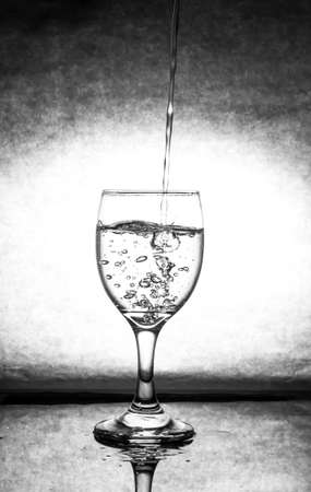 Pour water into the wine glass, creating bubbles in the water, which are placed on the glass floor, with the shadow of the glass reflecting the black background with the light in the center of the image.の写真素材
