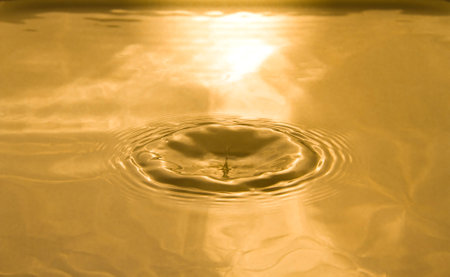 The waves caused by water droplets form a hole in the water and a beautiful reflection from the golden evening light.の写真素材