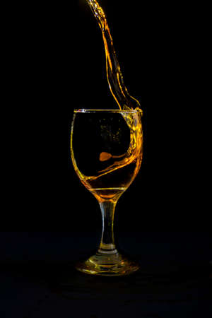 Pour the orange water from the glass into the crystal wine glass, spread it closely on a black background.の写真素材
